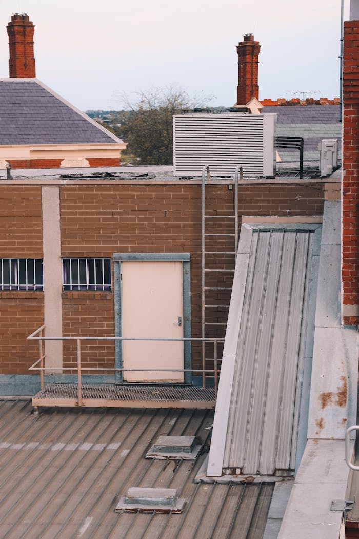 View of an urban rooftop with brick buildings, HVAC unit and ladder.